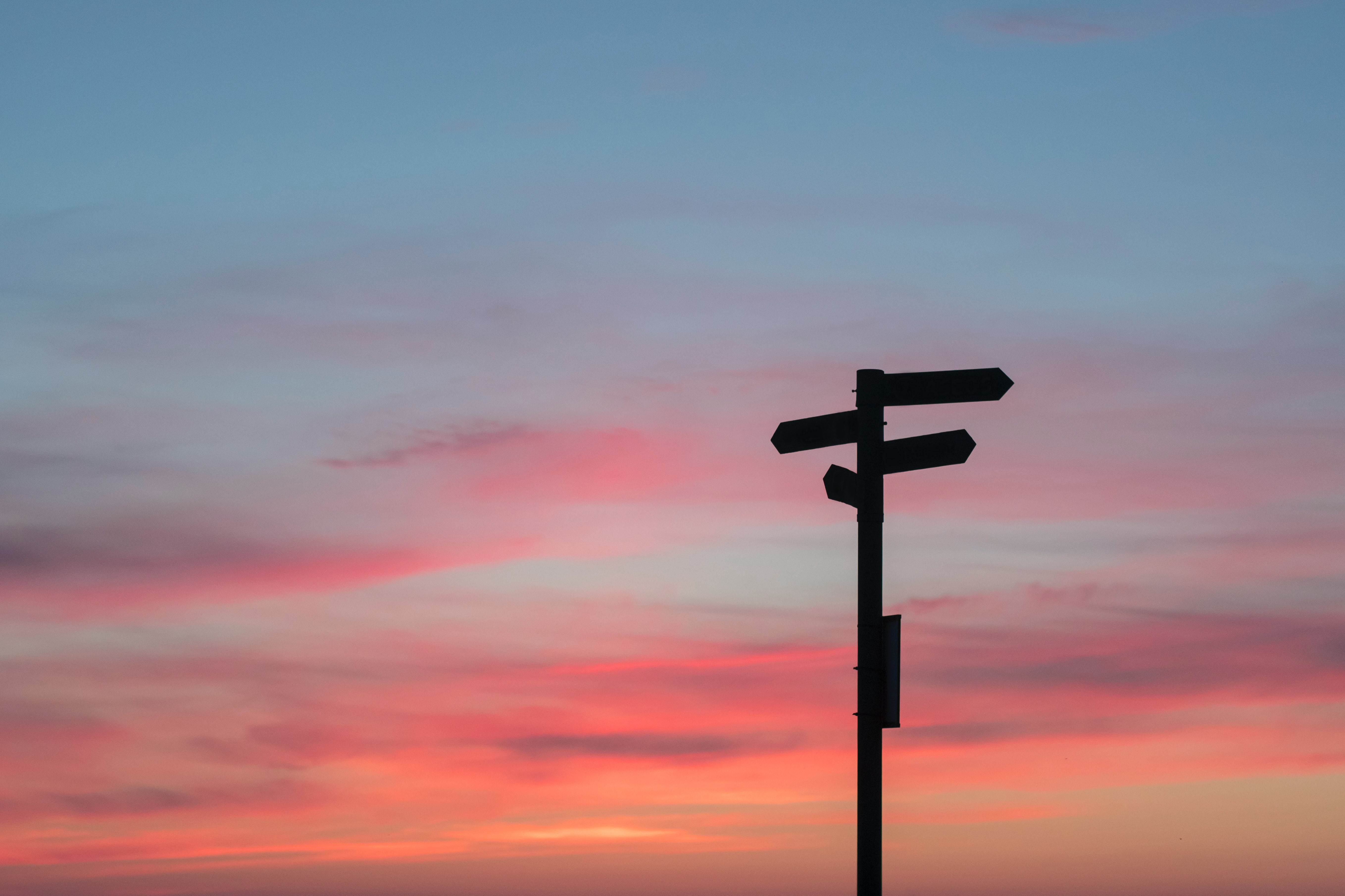 blue and pink sky with sunset and one pole with road signs pointing in many directions